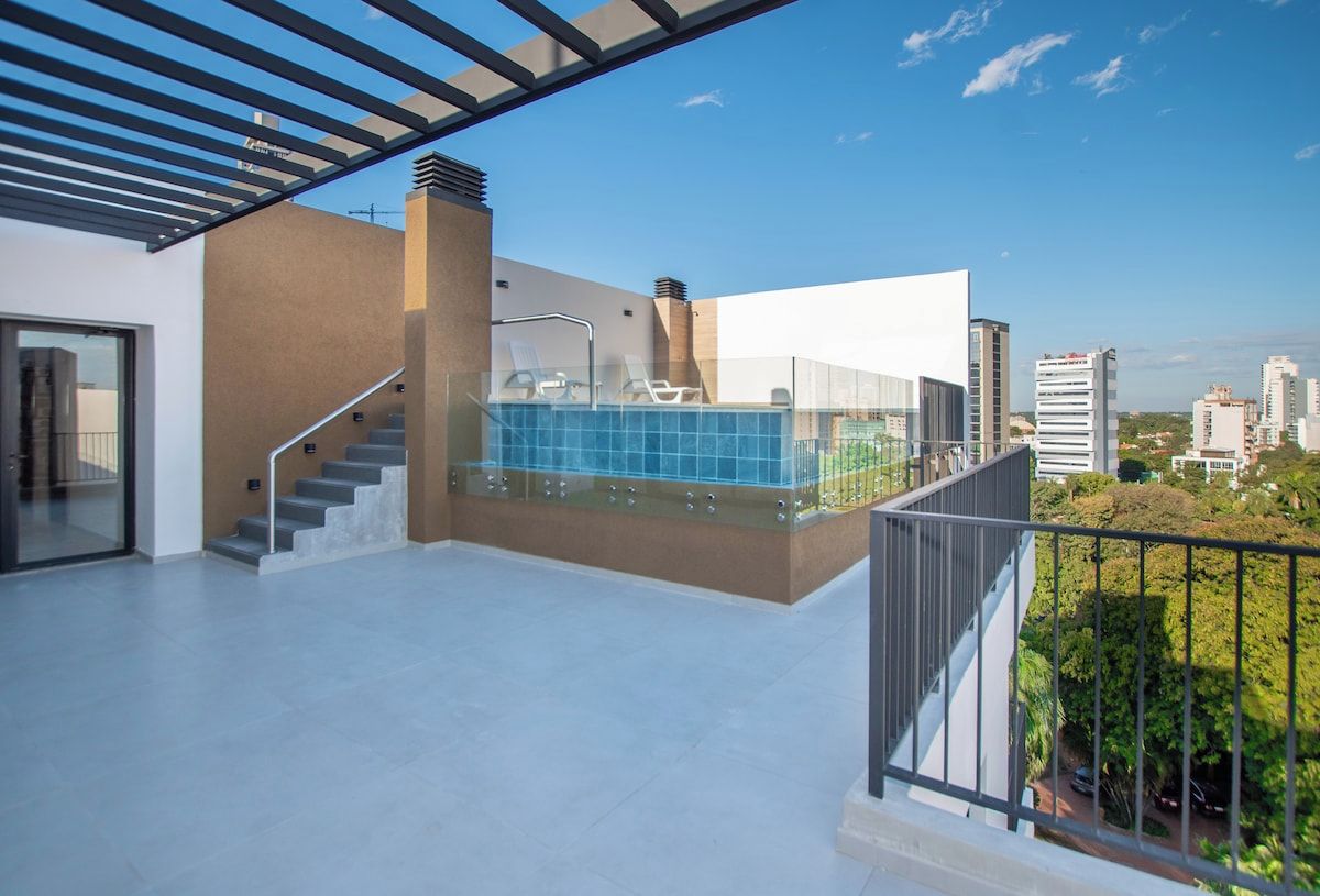 Terraza en la azotea con piscina, barandilla de cristal y vistas a la ciudad.