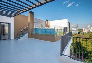Terrassa al terrat amb piscina, barana de vidre i vista a la ciutat.