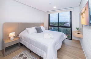 A modern hotel room with a large bed, bedside lamp, and a view of the city through a large window. - Cozy Central Stay Near Top Malls with Pool and Gym (Asunción)