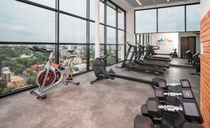 A gym with exercise equipment, large windows, and a city view. - Cozy Central Stay Near Top Malls with Pool and Gym (Asunción)
