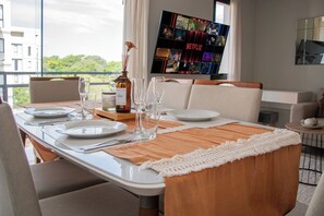 A dining area with a table set for four, a television displaying Netflix content, and a view of greenery outside. - Business Living, Pool & Workspace, Malls Nearby (Luque)