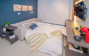 Ein Schlafzimmer mit Bett, Nachttisch, Lampe und einem an der Wand befestigten Fernseher.
