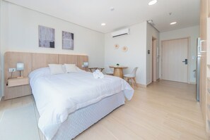 A hotel room with a large bed, bedside tables, a small round table, and a chair. - Modern Studio with Rooftop Pool, Gym & 200 Mbps WiFi (Asunción)