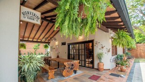 A wooden outdoor seating area with a bench and table, surrounded by potted plants and a hanging fern. - 4BR Home | Private Pool, Jacuzzi & BBQ (San Bernardino)