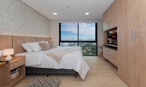 A modern bedroom with a large bed, a TV cabinet, and a city view. - Bright Studio with Gym,Rooftop Pool and City Views (Asunción)