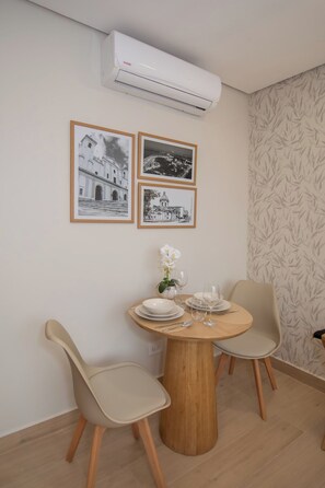 Ein Essbereich mit einem runden Tisch, zwei Stühlen, einer weißen Orchidee und drei gerahmten Schwarz-Weiß-Fotos an der Wand.