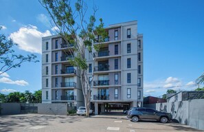 Ein mehrgeschossiges Wohngebäude mit Balkonen, einem Parkplatz und blauem Himmel.