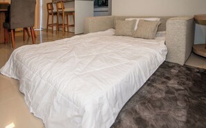 A bedroom with a large bed, a sofa, and a dining area with chairs. - Luque 2BR | Near Airport, Balcony & Parking (Luque)