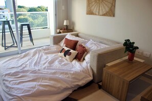 Ein Schlafzimmer mit Bett, Nachttisch, Lampe und Blick ins Freie.