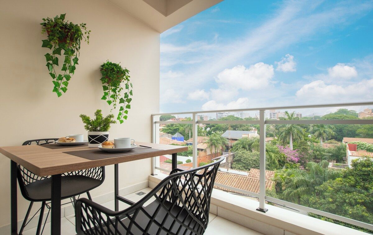 A balcony with a table, chairs, and hanging plants.