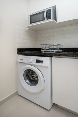A compact laundry room with a front-loading washing machine, a microwave above it, and a dish rack on the countertop. - Charming Corporate Hub with Pool, Gym & Workspace (Asunción)