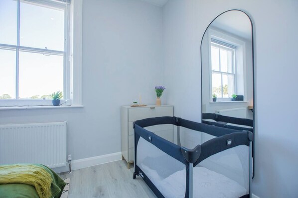 Una habitación con literas, un radiador, una ventana con plantas y un espejo.
