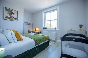 A bedroom with a bed, a crib, a window, a radiator, and a painting on the wall.
