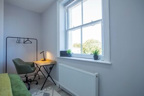 A room with a desk, chair, radiator, window, and a plant.