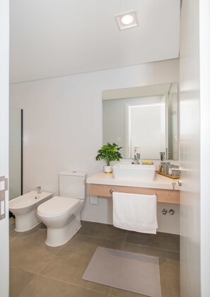 Ein modernes Badezimmer mit Toilette, Bidet, Waschbecken und Spiegel.