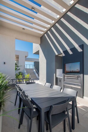 Um pátio externo com mesa e cadeiras, churrasqueira embutida e vista para o horizonte da cidade.