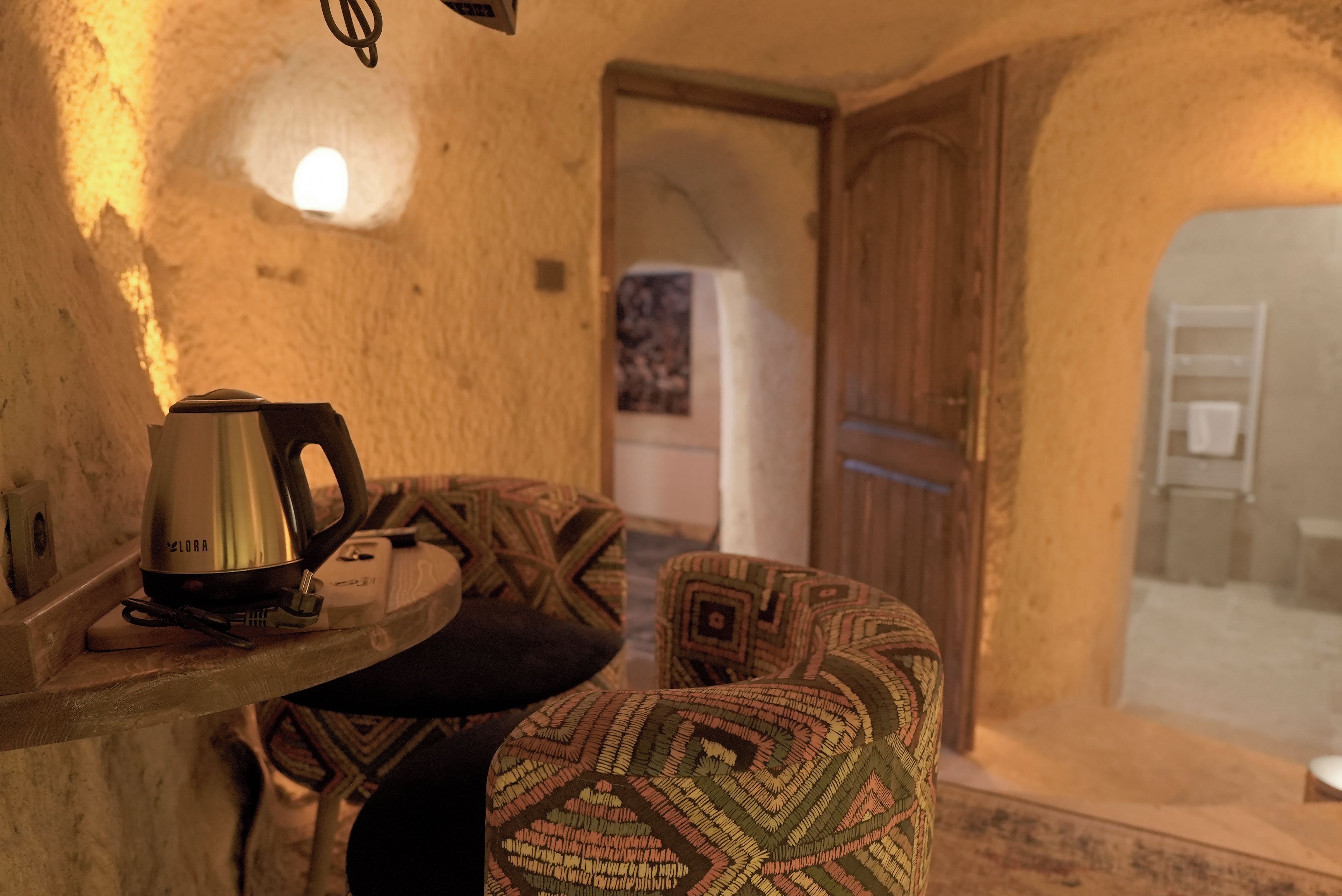 Un interior acogedor con una pared de piedra rústica, una pequeña mesa con una tetera y un cojín estampado.