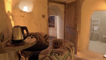 Un interior acogedor con una pared de piedra rústica, una pequeña mesa con una tetera y un cojín estampado.