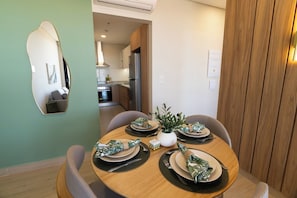 A dining area with a round table set for four, a mirror on the wall, and a kitchen in the background. - One-BR with Balcony Near Malls, Pool & City Views (Asunción)