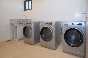 A laundry room with three front-loading washing machines, a countertop, and a sink. - One-BR with Balcony Near Malls, Pool & City Views (Asunción)
