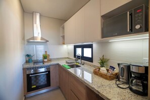 A modern kitchen with a stainless steel range hood, a built-in oven, a microwave, and a coffee maker. - One-BR with Balcony Near Malls, Pool & City Views (Asunción)