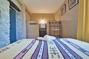 Una habitación con una cama, una estantería metálica, una puerta y una lámpara fijada a la pared.
