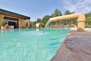 A swimming pool with a water feature, surrounded by a stone wall and greenery. - Private Villa & Nature - Domaine l'Oliveraie (Essaouira)