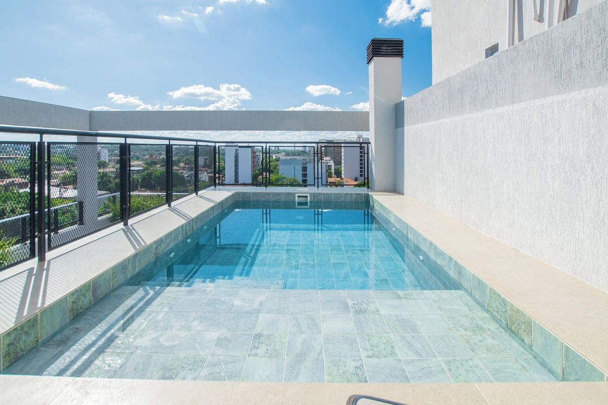 Piscina en la azotea con vistas a edificios y un cielo despejado.