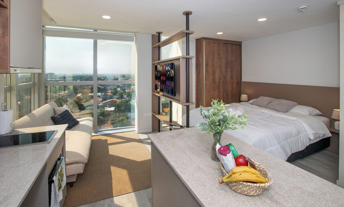 A modern hotel room with a balcony, a bed, a TV, and a breakfast bar.