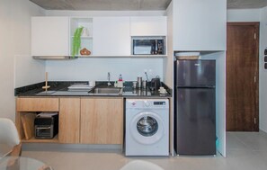 A compact kitchen with a built-in washing machine, a microwave, and a refrigerator. - Stylish City Escape with Panoramic Views, Pool&Gym (Asunción)