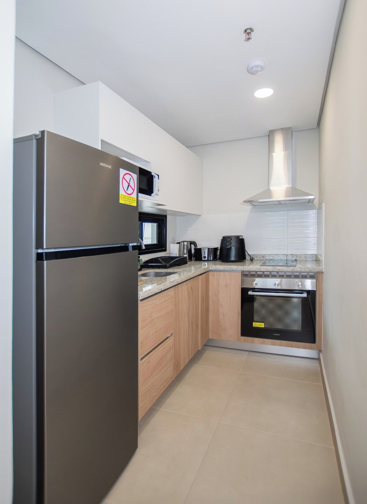 Eine moderne Küche mit Kühlschrank aus Edelstahl, Mikrowelle, Wasserkocher, Kaffeemaschine und Backofen.
