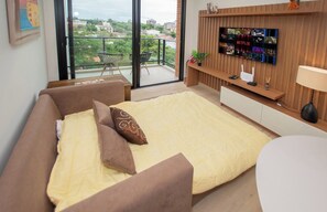 Un dormitorio moderno con una cama grande, un televisor montado en la pared y un balcón con vistas a la ciudad.