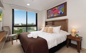 A hotel room with a large bed, a desk, a chair, a nightstand with a lamp, and a painting on the wall. - Matrisa 1BR | Balcony, Rooftop Pool & Gym (Asunción)