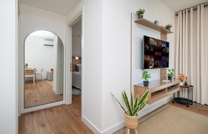 Un salon moderne avec un téléviseur à écran plat fixé sur une étagère en bois, un miroir au mur et une plante en pot posée sur le sol.