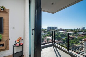 A balcony with a city view, a small table with a vase of flowers, and a mounted TV. - Prime Location One-Bedroom Near the Mall (Asunción)
