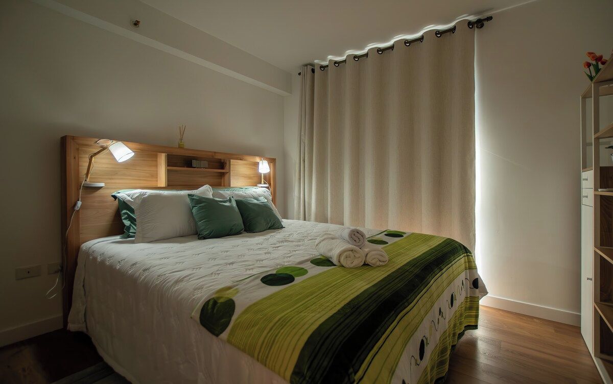 A neatly made bed with a headboard, a bedside lamp, and a rolled towel on the bed.