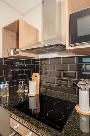 A modern kitchen with a black tiled backsplash, stainless steel appliances, and wooden cabinetry. - Modern 1BR in Boggiani | Pool, City Views & WiFi (Asunción)