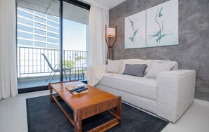A modern living room with a sofa, a coffee table, and a floor lamp. There is a balcony with a railing and a view of buildings. - Stylish City Apartment with Balcony, Pool and Gym (Asunción)