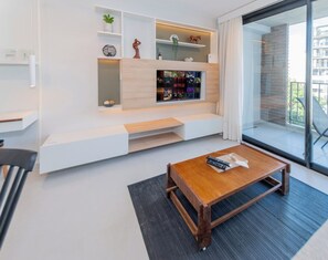 A modern living room with a built-in entertainment unit, a wooden coffee table, and a large window offering a view of the outdoors. - Stylish City Apartment with Balcony, Pool and Gym (Asunción)