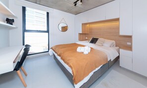 A modern bedroom with a bed, bedside table, and a desk with a chair. - Stylish City Apartment with Balcony, Pool and Gym (Asunción)