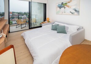 A bedroom with a large bed, a view of the city through a glass door, and a small table with a lamp. - Matrisa 1BR Asunción | Pool, Gym & Balcony (Asunción)
