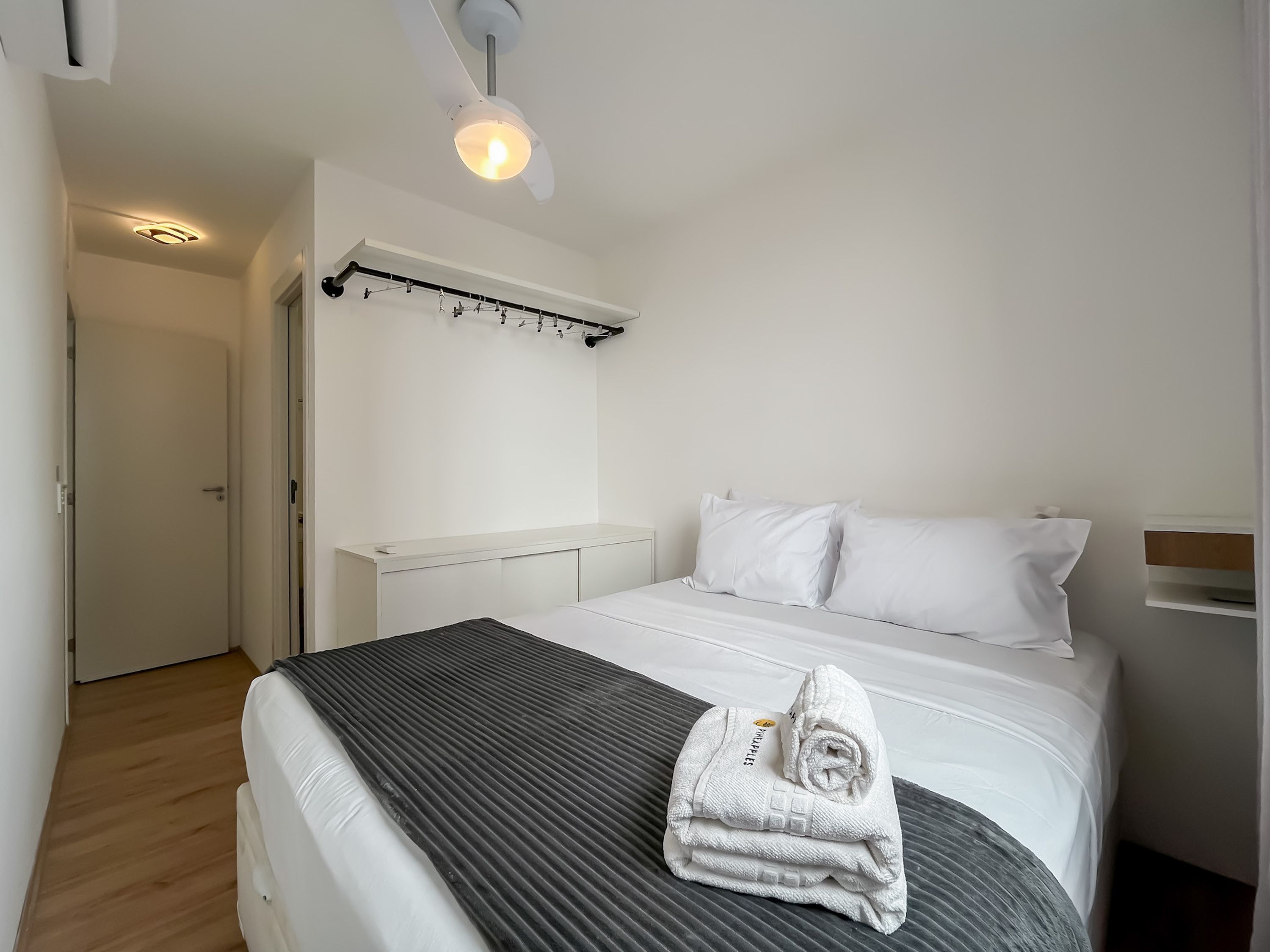 A hotel room with a bed, a bedside table, a wall-mounted light fixture, and a door.