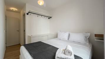 A hotel room with a bed, a bedside table, a wall-mounted light fixture, and a door.
