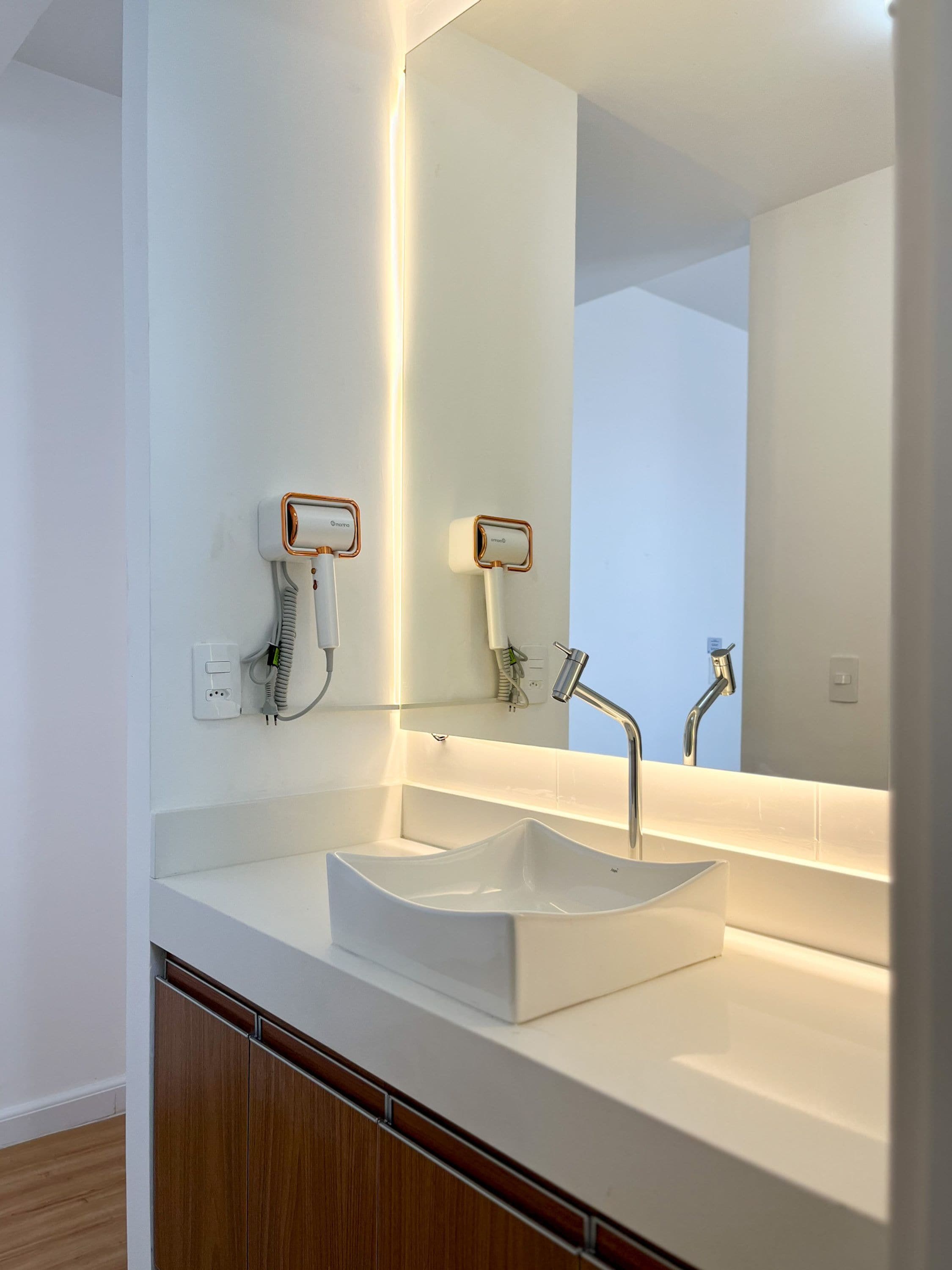 A modern bathroom with a white sink, a large mirror, and a towel rack.