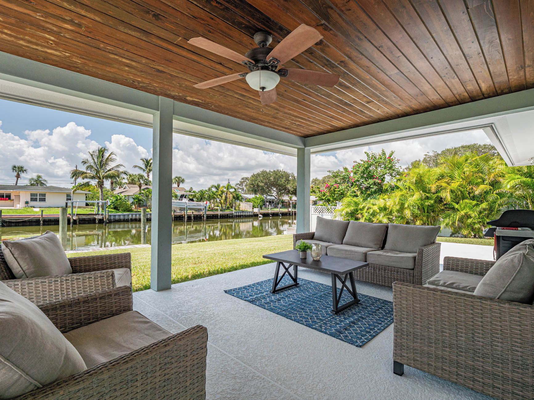 An outdoor patio with wicker furniture, a ceiling fan, and a view of a water body and greenery.