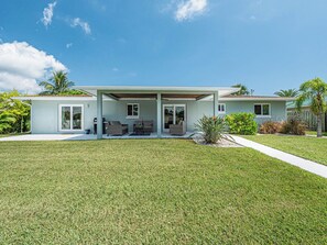A modern two-story house with a covered patio area, a lawn, and tropical landscaping. - Waterfront 3BR home with private dock, down the street from the beach! (Fort Pierce)