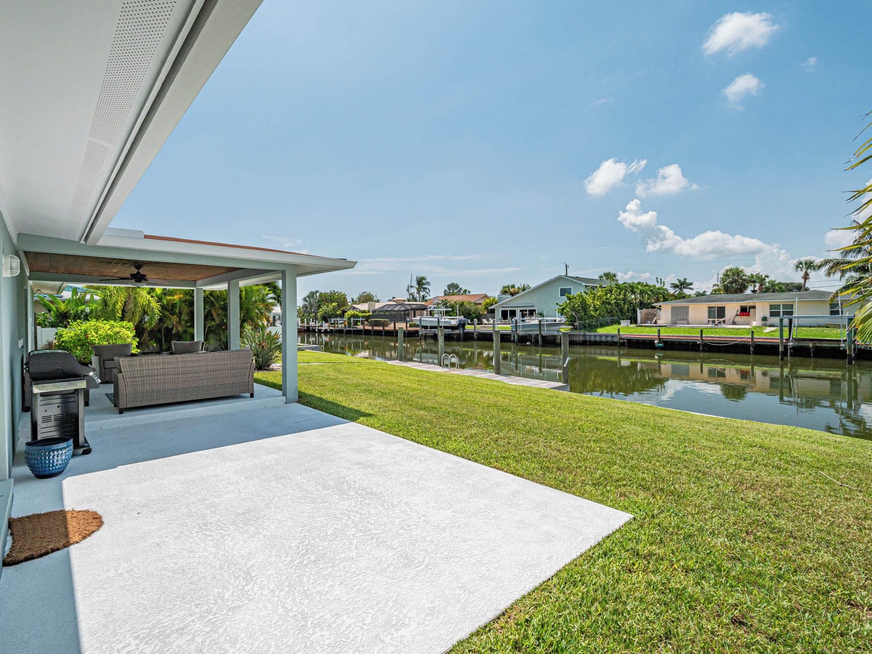 A covered patio with outdoor furniture, a view of a canal, and a grassy area.