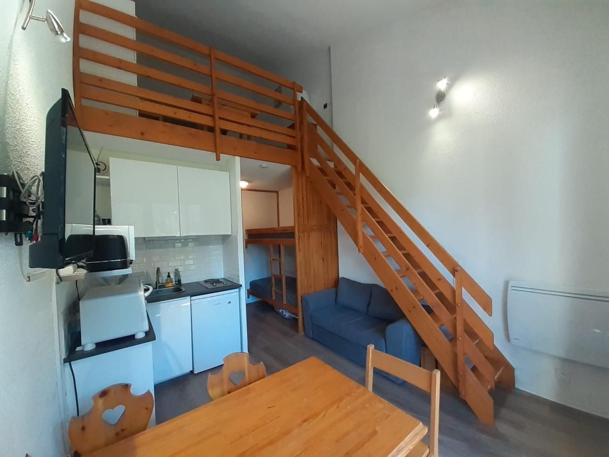Un espace de vie compact comprenant une cuisine, un coin repas et une chambre en mezzanine accessible par un escalier en bois.