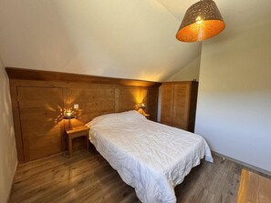 Ein Schlafzimmer mit einem hölzernen Kopfteil, einem Einzelbett mit weißer Bettwäsche, zwei Nachttischlampen und einer Pendelleuchte.