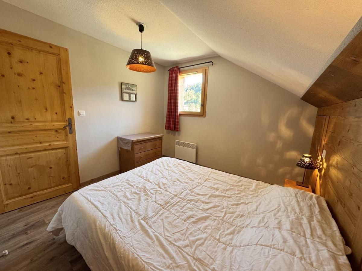 Une chambre à coucher avec un lit, une armoire en bois, une commode, un radiateur, une fenêtre avec un rideau rouge et une lampe suspendue.